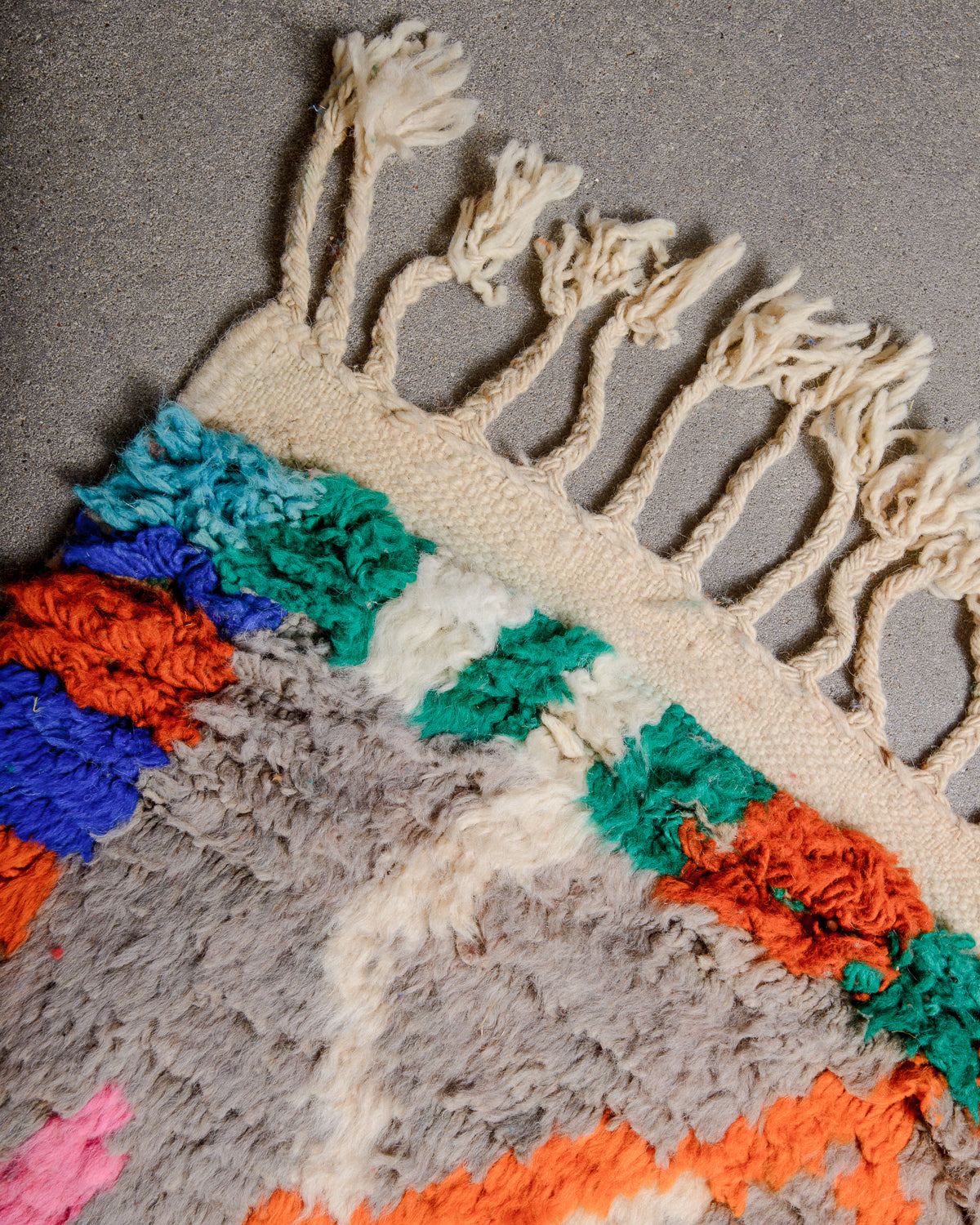 Corner of Berber runner rug with brightly coloured wool pile and natural wool tassels.